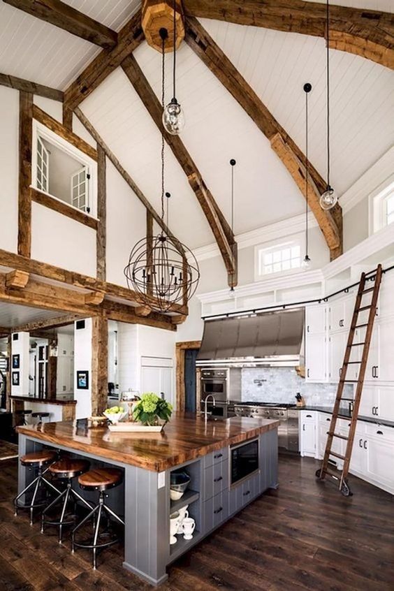 a barn kitchen with wooden beams, white shaker style cabinets, a grey planked kitchen island that doubles as a table