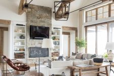 a barn living room with woodenn beams, white planked walls, a fireplace clad with stone, neutral seating furniture, leather chairs and baskets