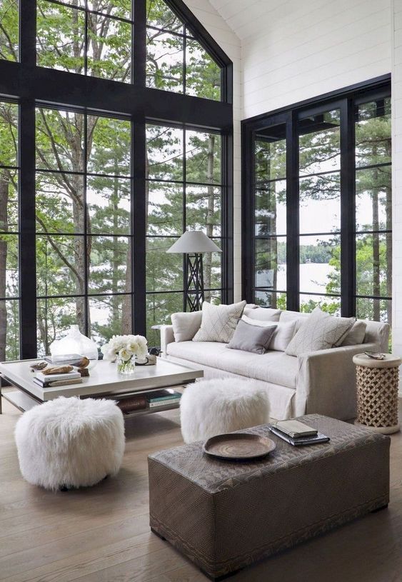 a beautiful barn living room with double-height windows, neutral furniture and a brown ottoman, faux fur stools is amazing