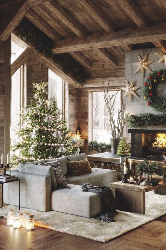 a beautiful barn living room with wooden walls, a ceiling and wooden beams, a fireplace clad with concrete, a low sectional, a wooden bench, a Christmas tree and arrangements
