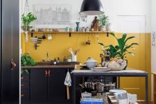 a black modern kitchen with a mustard painted backsplash, an open shelf anda metal kitchen island plus potted plants