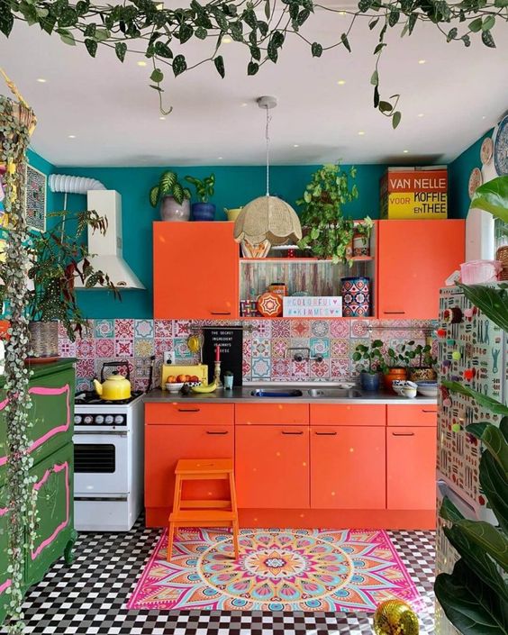 a bright orange kitchen with colorful mismatching tiles, bleu walls, a green sideboard, potted plants and a colorful rug