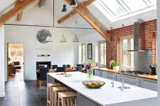 a contemporary barn kitchen with skylights, dove grey plain cabinets, butcherblock countertops, wooden beams, black pendant lamps