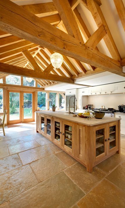 a cozy barn kitchen with wooden beams on the ceiling, white cabinets, a light stained kitchen island, a crystal chandelier and a tile floor