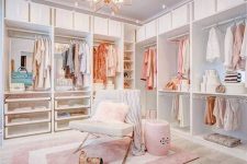 a glam feminine closet with open storage units, drawers, a pink chandelier, a chair and a side table plus a pink printed rug