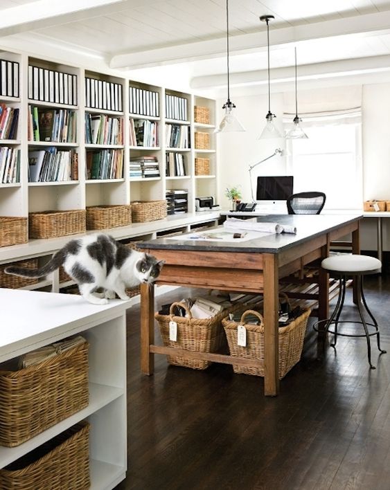 a large creative studio with an overiszed bookcase with baskets for storage, an oversized table and baskets underneath, stools and pendant lamps