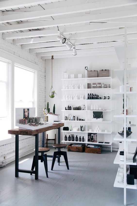 a light-filled home artist studio with white open shelves, a tall desk and stools, some art and a lot of supplies