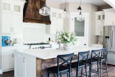 a modern barn kitchen with white cabinets and a kitchen island, with a reclaimed wood hood and black stools, glass pendant lamps