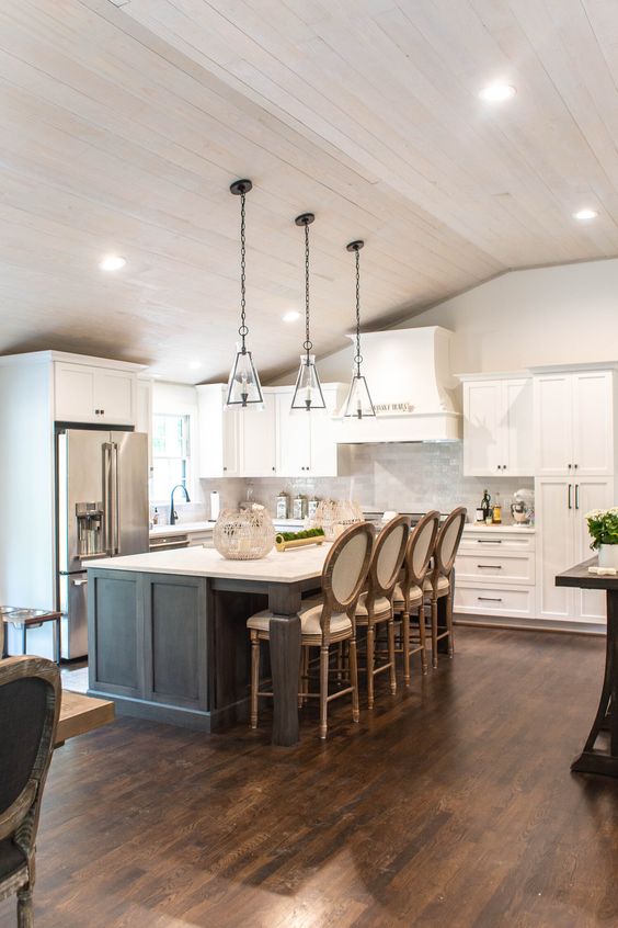 a modern barn kitchen with white shaker style cabinets, a grey kitchen island with a dining space, glass pendant lamps and lights