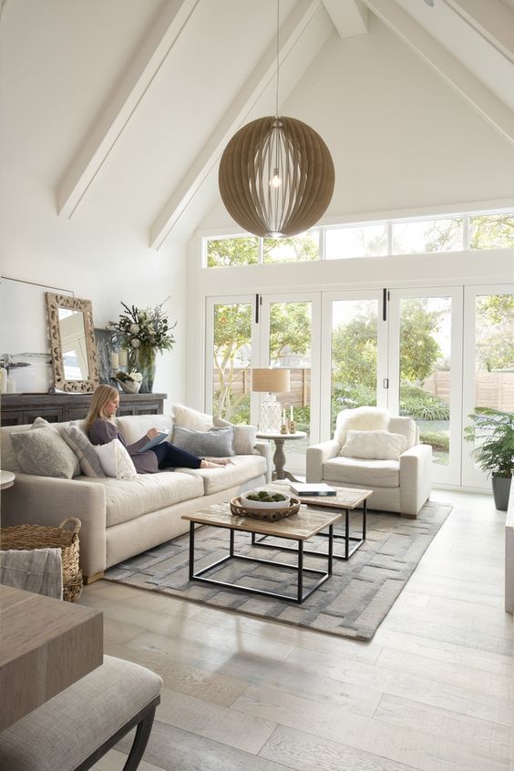 a modern neutral barn living room with neutral seating furniture, a sphere pendant lamp, a dark sideboard and lovely views of the garden