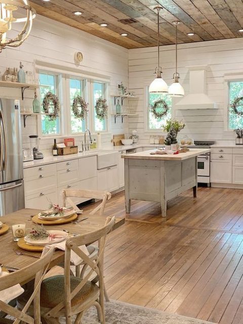 a neutral barn kitchen with planked walls, a reclaimed wood ceiling, white cabinets and a shabby chic kitchen island, pendant lamps