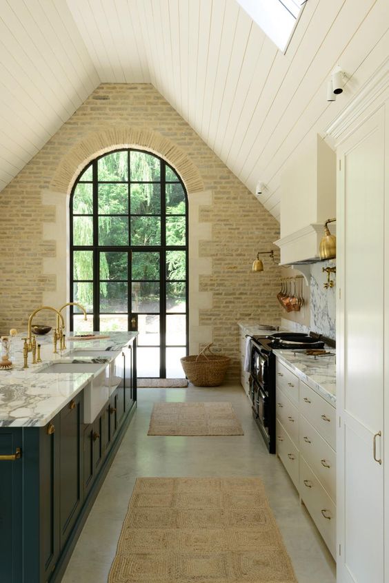 a neutral barn kitchen with white cabinets, a teal kitchen island, white marble countertops and a white stone wall