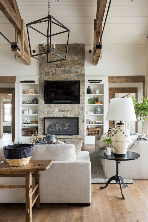 a neutral barn living room with a built-in fireplace, neutral seating furniture, wooden beams, a metal chandelier and baskets