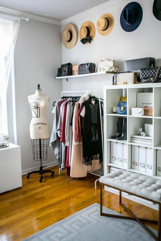 a pretty neutral closet with a makeshirt part, open storage shelves, a tufted bench, hats as decor and a printed rug is amazing