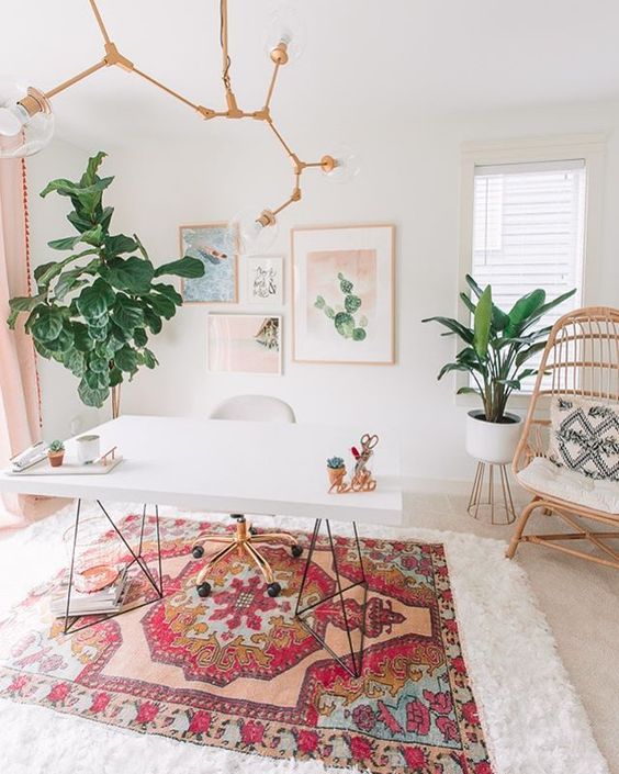 a romantic boho home office with a printed rug and pillows, a pastel gallery wall, a gold chandelier and pink curtains