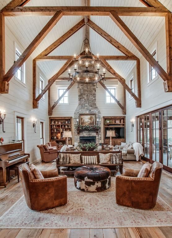 a rustic barn living room with wooden beams and white planked walls and a ceiling, leather furniture, a metal tiered chandelier and neutral textiles