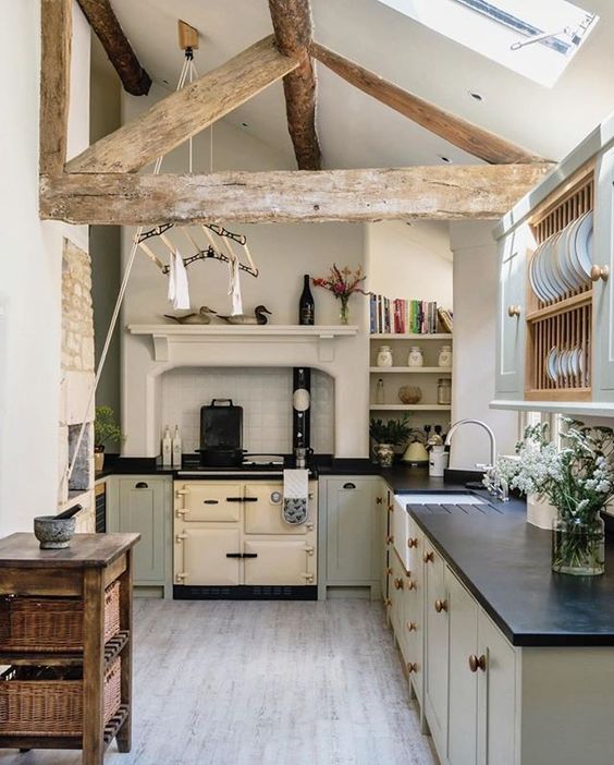a small and cozy barn kitchen in neutrals, with a skylight, a reclaimed wooden beam, dove grey kitchen cabinets with black countertops and a wooden kitchen island