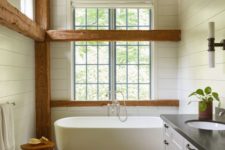 a white barn bathroom with wooden beams, a wooden ceiling with beams, a free-standing tub, vintage furniture