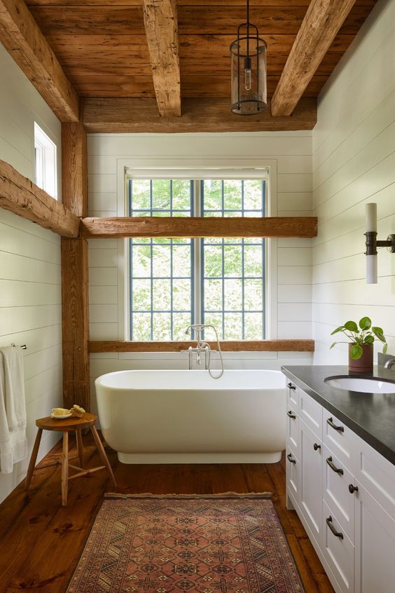 a white barn bathroom with wooden beams, a wooden ceiling with beams, a free-standing tub, vintage furniture