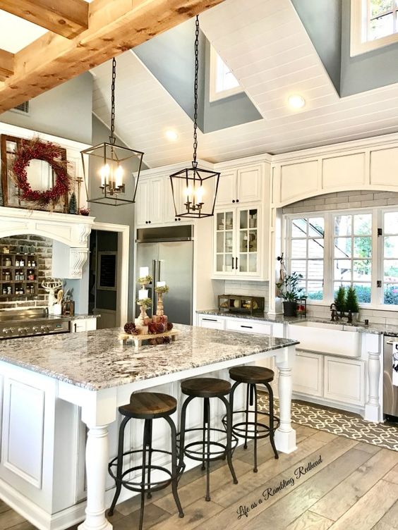 a white barn kitchen with skylights and wooden beams, white shaker cabinets and a large kitchen island, vintage black pendant lamps