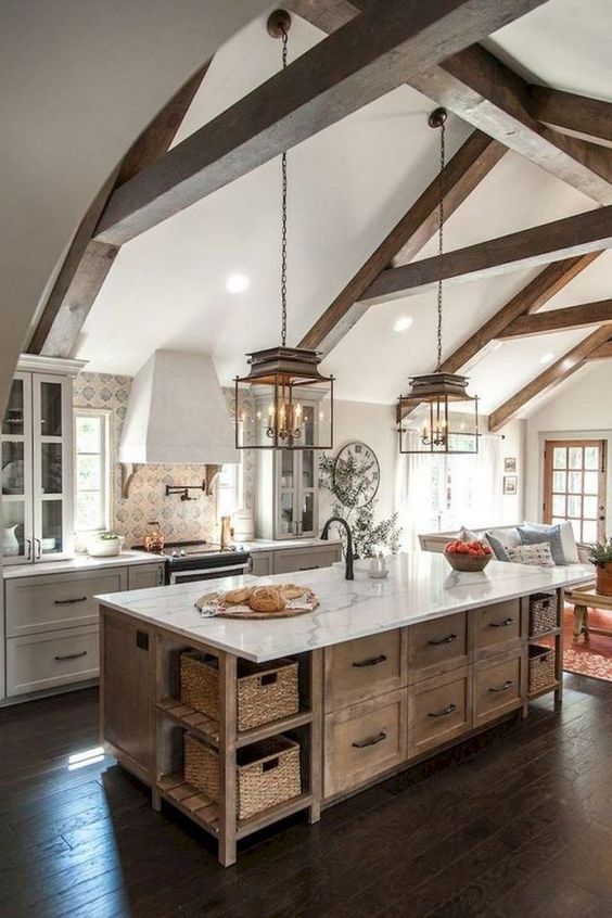 an elegant barn kitchen with wooden beams, white shaker style cabinets, a stained kitchen island, vintage pendant lamps