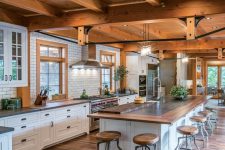 an inviting barn kitchen with a wooden ceiling and beams, white shaker style cabinets and a matching kitchen island and potted plants