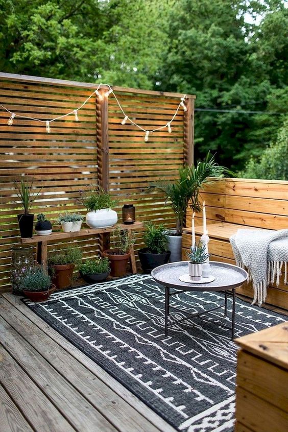 a backyard deck with built-in benches, potted greenery, lights and a screen for privacy is a great space to spend time