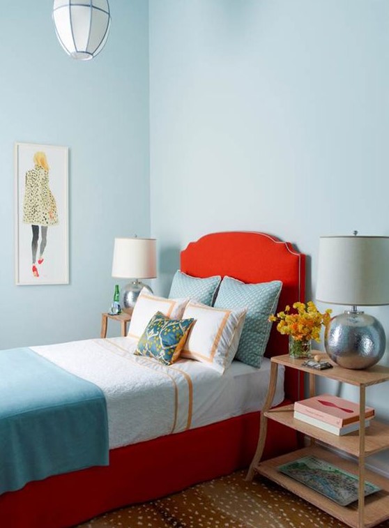 a beautiful bedroom with light blue walls, a red upholstered bed, printed and pastel bedding, wooden nightstands and silver table lamps