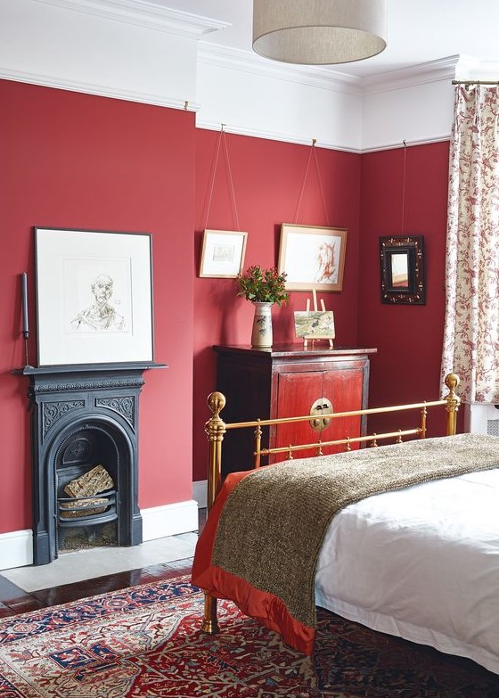 a beautiful vintage bedroom with red walls, a gold bed, a redwood dresser, chic artworks and a built-in fireplace