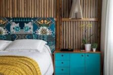 a bold and catchy bedroom with rich-stained panels on the walls, a bed with a printed headboard, a turquoise dresser, a wooden pendant lamp