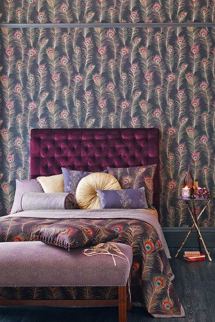 a bold bedroom with a peacock feather wall, a bold purple bed and a purple bench, colorful pillows and a nightstand
