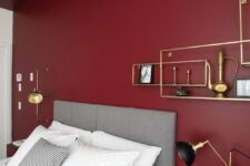a bold modern bedroom with a burgundy accent wall, a grey bed, black nightstands and touches of gold or a chic look