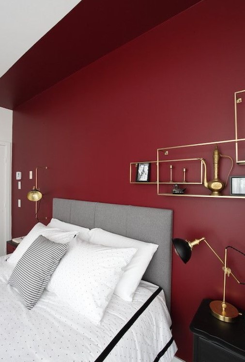 a bold modern bedroom with a burgundy accent wall, a grey bed, black nightstands and touches of gold or a chic look