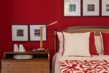 a bold red bedroom with a rattan bed and red and white bedding, a stained nightstand and gallery walls