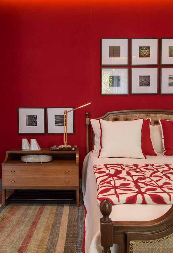 a bold red bedroom with a rattan bed and red and white bedding, a stained nightstand and gallery walls