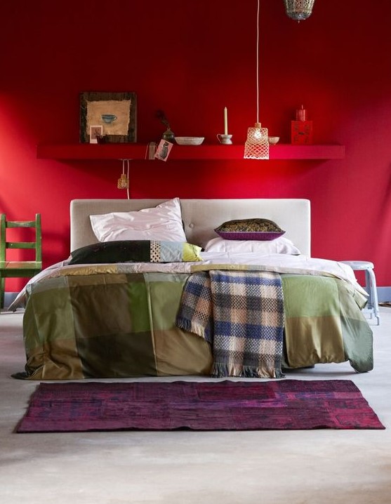 a bright red eclectic bedorom with a shelf over the bed, a white bed with printed bedding, accessories and decor and a pendant lamp