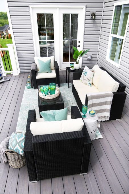 a bright summer deck with dark wicker furniture, neutral and light colored textiles and potted greenery is very welcoming