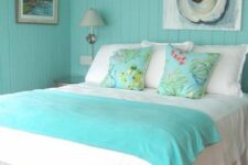 a brigth bedroom with turquoise shiplap walls, a bed with turquoise and white bedding, nightstands and some art