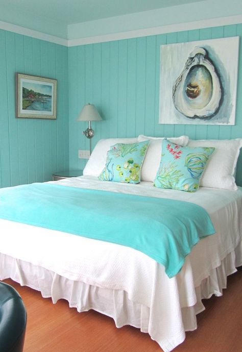 a brigth bedroom with turquoise shiplap walls, a bed with turquoise and white bedding, nightstands and some art