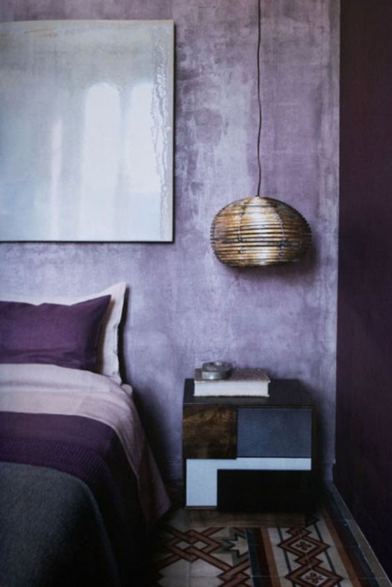 a catchy bedroom with a purple and watercolor lavender wall, purple and pink bedding, a shiny pendant lamp