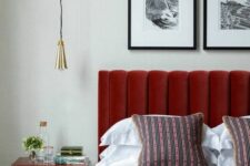 a chic bedorom with a red upholstered bed, bright and printed bedding, a deep red nightstand and a pendant lamp