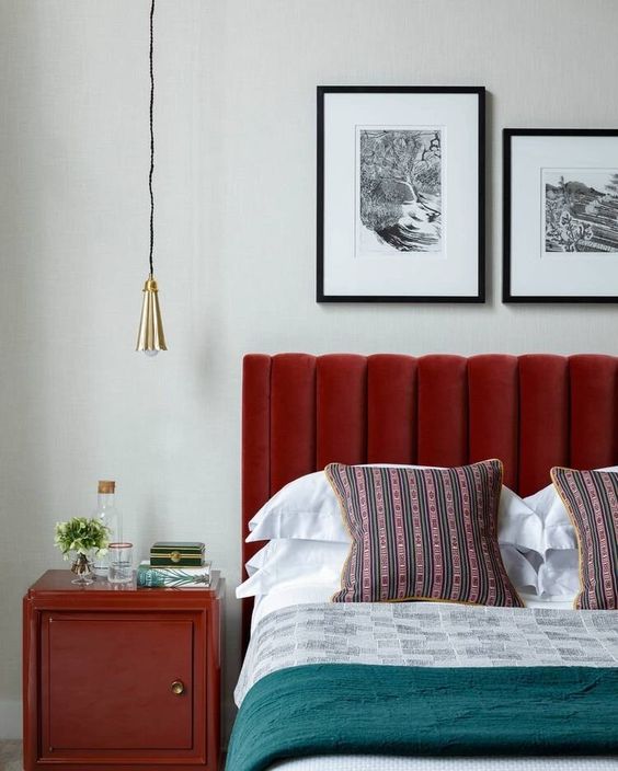 a chic bedorom with a red upholstered bed, bright and printed bedding, a deep red nightstand and a pendant lamp