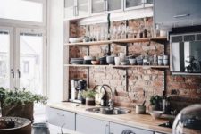 a chic kitchen with blue cabinets, light-colored countertops and a red brick wall looks very refreshing