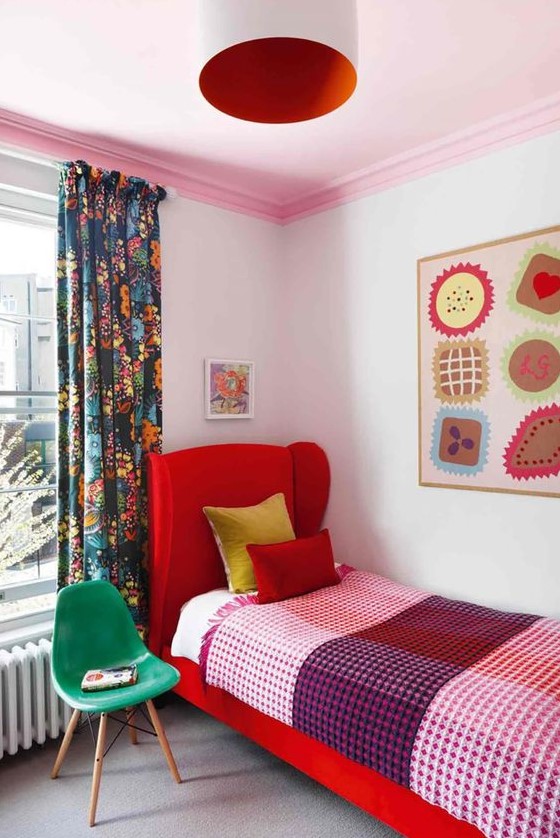 a colorful guest bedroom with a red upholstered bed, colorful bedding, a bright artwork, a white and red pendant lamp and a green chair