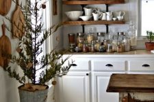 a country cottage kitchen with white cabinets, open shelves, cutting boards on the wall, a shabby chic kitchen island that is a table