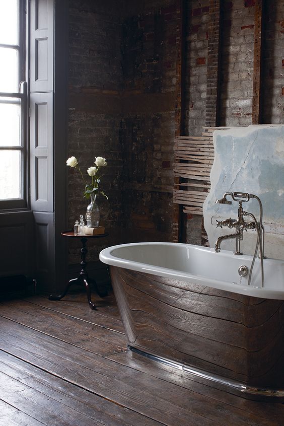 a dark industrial bathroom with red brick walls, dark wooden floora and a chic metal bathtub for a refined look