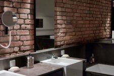 a dark minimalist bathroom with marble tiles, a dark vanity and a red brick wall that adds texture and interest