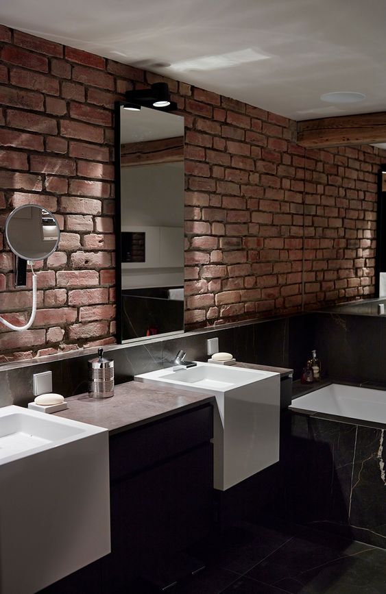 a dark minimalist bathroom with marble tiles, a dark vanity and a red brick wall that adds texture and interest