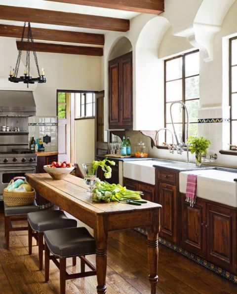 a dark-stained shaker style kitchen with dark stone countertops, a ceiling with dark beams, a vintage stained table that doubles as a kitchen island