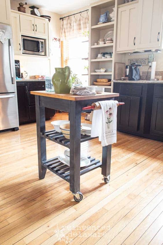 a farmhouse kitchen with black and white cabinets, stone countertops, a tiny black vintage kitchen island on casters that perfectly matches